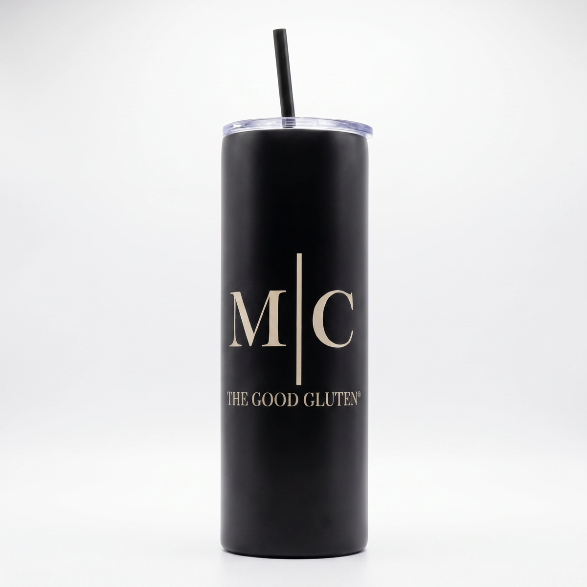 A matte black insulated tumbler with a clear lid and black straw, featuring the gold printed initials 'M|C' and the text 'THE GOOD GLUTEN' on the front, set against a plain white background.